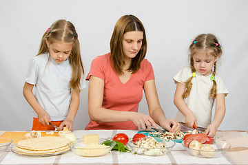 Image showing Mom teaches two daughters to cook. It helps them to cut mushrooms and vegetables