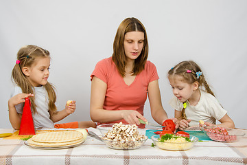 Image showing Mom shows two young daughters at the kitchen table as the cut tomato pizza