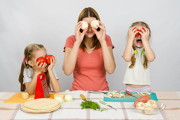 Image showing Mum with two little girls having fun at the kitchen table playing with vegetables