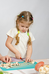 Image showing Little girl stands at the kitchen table and helps chop the mushrooms with a knife