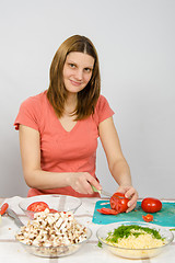 Image showing The girl at the kitchen table cutting the tomato