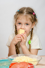 Image showing Five-year girl with pigtails eating cheese at the table in front of her is a plate of grated cheese