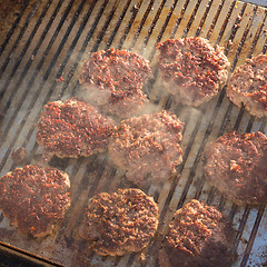 Image showing Beef burgers being grilled on food stall grill.