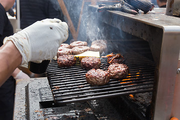 Image showing Beef burgers being grilled on food stall grill.