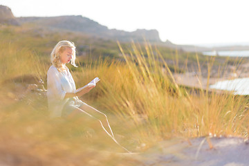 Image showing Woman enjoys reading on beautiful sandy beach.