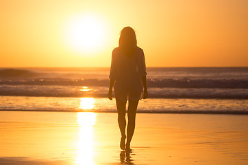 Image showing Lady walking on sandy beach in sunset.