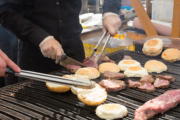 Image showing Beef burgers being grilled on food stall grill.