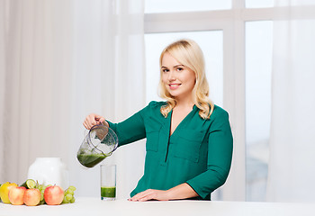 Image showing happy woman with blender jug pouring juice at home