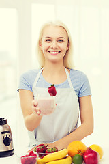 Image showing smiling woman holding glass of fruit shake at home