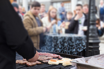 Image showing Beef burgers being grilled on food stall grill.