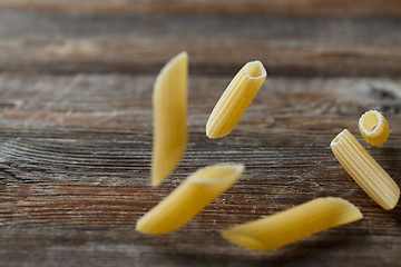 Image showing Falling penne pasta. Flying yellow raw macaroni over black background.