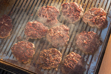 Image showing Beef burgers being grilled on barbecue.