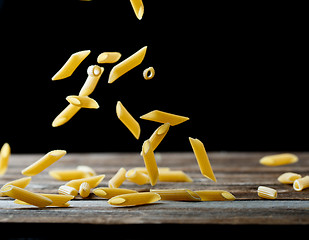 Image showing Falling penne pasta. Flying yellow raw macaroni over black background.