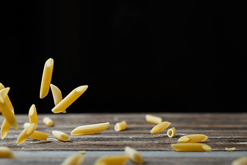 Image showing Falling penne pasta. Flying yellow raw macaroni over black background.