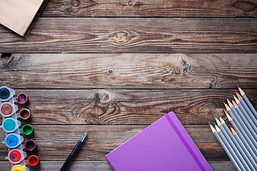 Image showing Watercolors, color pencils and sketchbook on wooden table. Flat lay photo with empty space for logo, text.