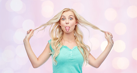 Image showing happy young woman showing tongue and holding hair