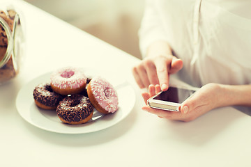 Image showing close up of hands with smart phone and donuts