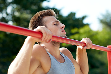 Image showing young man exercising on horizontal bar outdoors