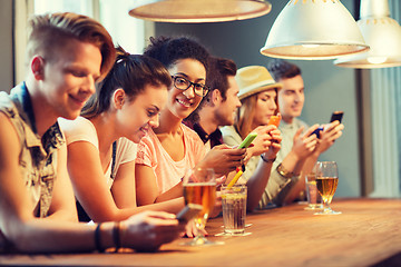 Image showing happy friends with smartphones and drinks at bar