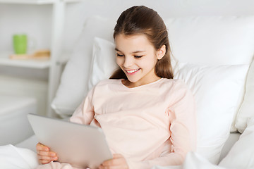 Image showing happy girl lying in bed with tablet pc at home