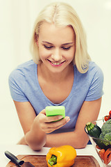 Image showing smiling woman with smartphone cooking vegetables