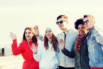 Image showing happy teenage friends waving hands on city street