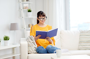 Image showing smiling young asian woman reading book at home