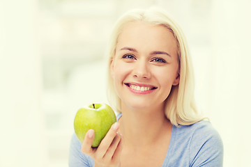 Image showing happy woman eating green apple at home