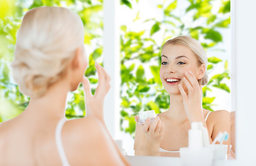 Image showing happy woman applying cream to face at bathroom