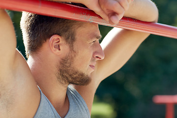 Image showing young man exercising on horizontal bar outdoors