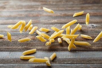 Image showing Falling penne pasta. Flying yellow raw macaroni over black background.