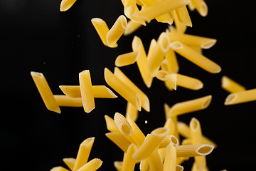 Image showing Falling penne pasta. Flying yellow raw macaroni over black background.