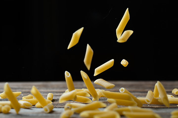 Image showing Falling penne pasta. Flying yellow raw macaroni over black background.