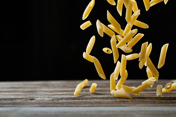 Image showing Falling penne pasta. Flying yellow raw macaroni over black background.