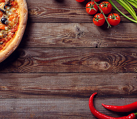 Image showing Italian pizza with tomatoes on a wooden table, top view.