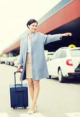 Image showing smiling young woman with travel bag catching taxi