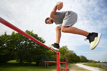 Image showing young man jumping on horizontal bar outdoors