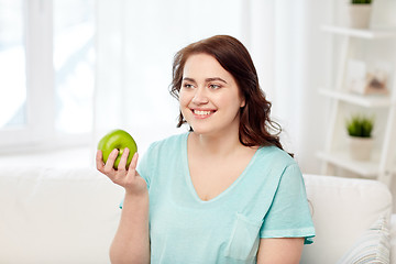 Image showing happy plus size woman eating green apple at home