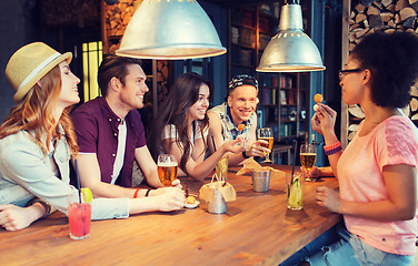 Image showing happy friends with drinks talking at bar or pub