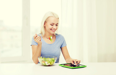 Image showing smiling woman eating salad with tablet pc at home