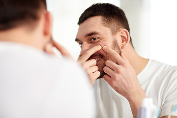 Image showing smiling man squeezing pimple at bathroom mirror