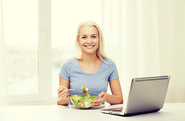 Image showing smiling woman eating salad with laptop at home