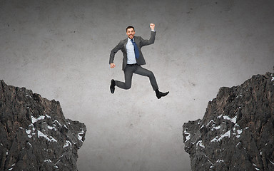 Image showing happy smiling businessman jumping between rocks