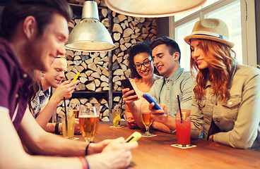 Image showing happy friends with smartphones and drinks at bar