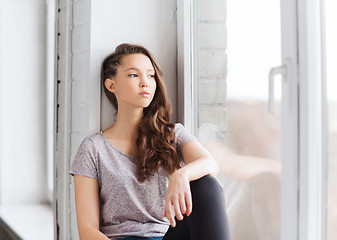 Image showing sad pretty teenage girl sitting on windowsill