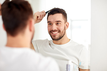 Image showing happy man brushing hair  with comb at bathroom