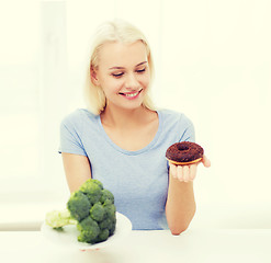 Image showing smiling woman with broccoli and donut at home