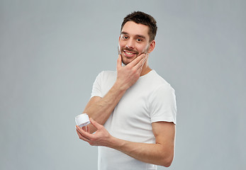 Image showing happy young man applying cream to face over gray