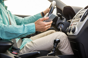 Image showing close up of man with smartphone driving car