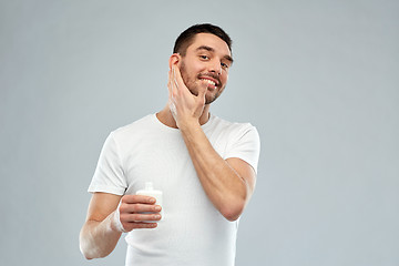 Image showing happy young man applying cream or lotion to face